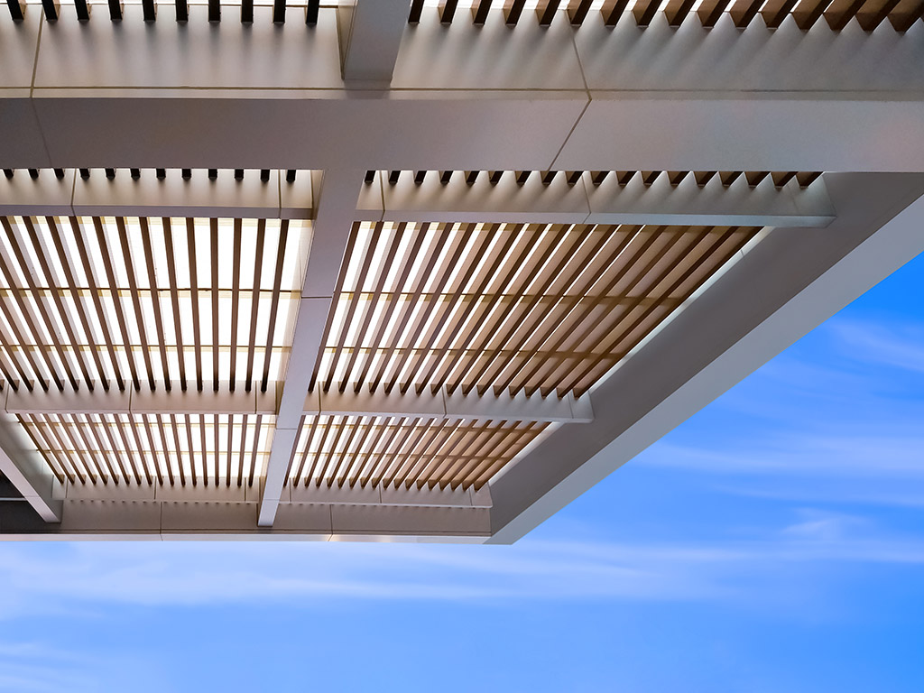 Low angle view of modern battens roof awning outside of building against blue sky background